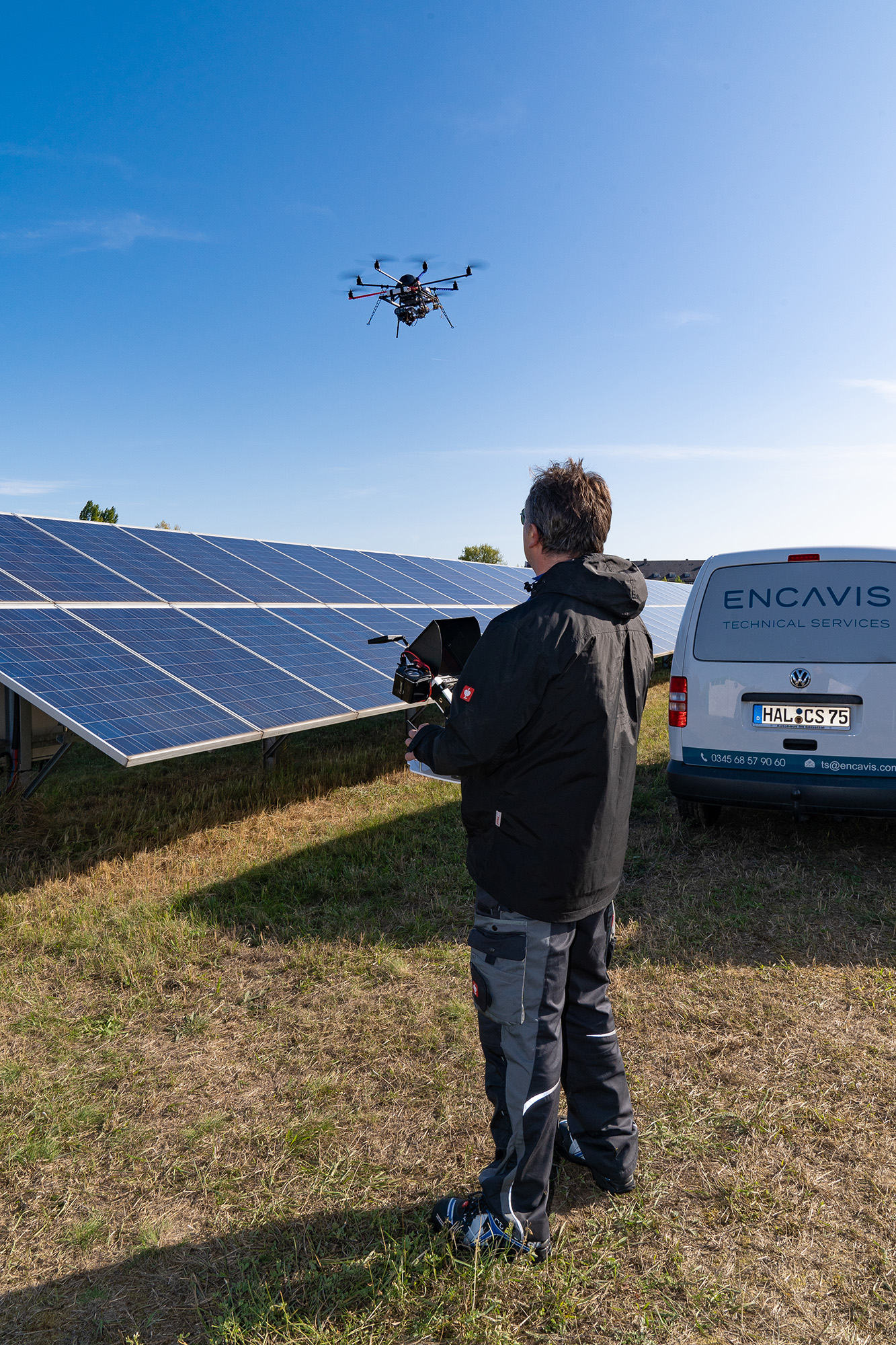 Drohneninspektion im Solarpark, Pilot steuert professionelle Drohne vor Solarmodulen