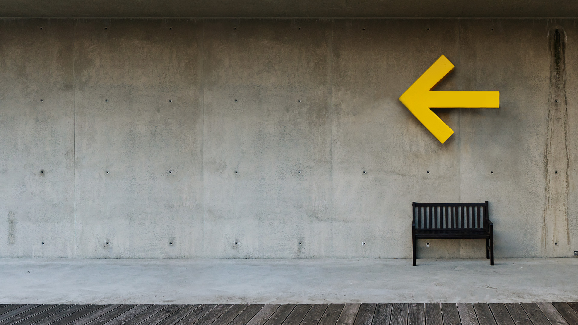 Gelber Pfeil an Betonwand, daneben eine dunkelbraune Bank