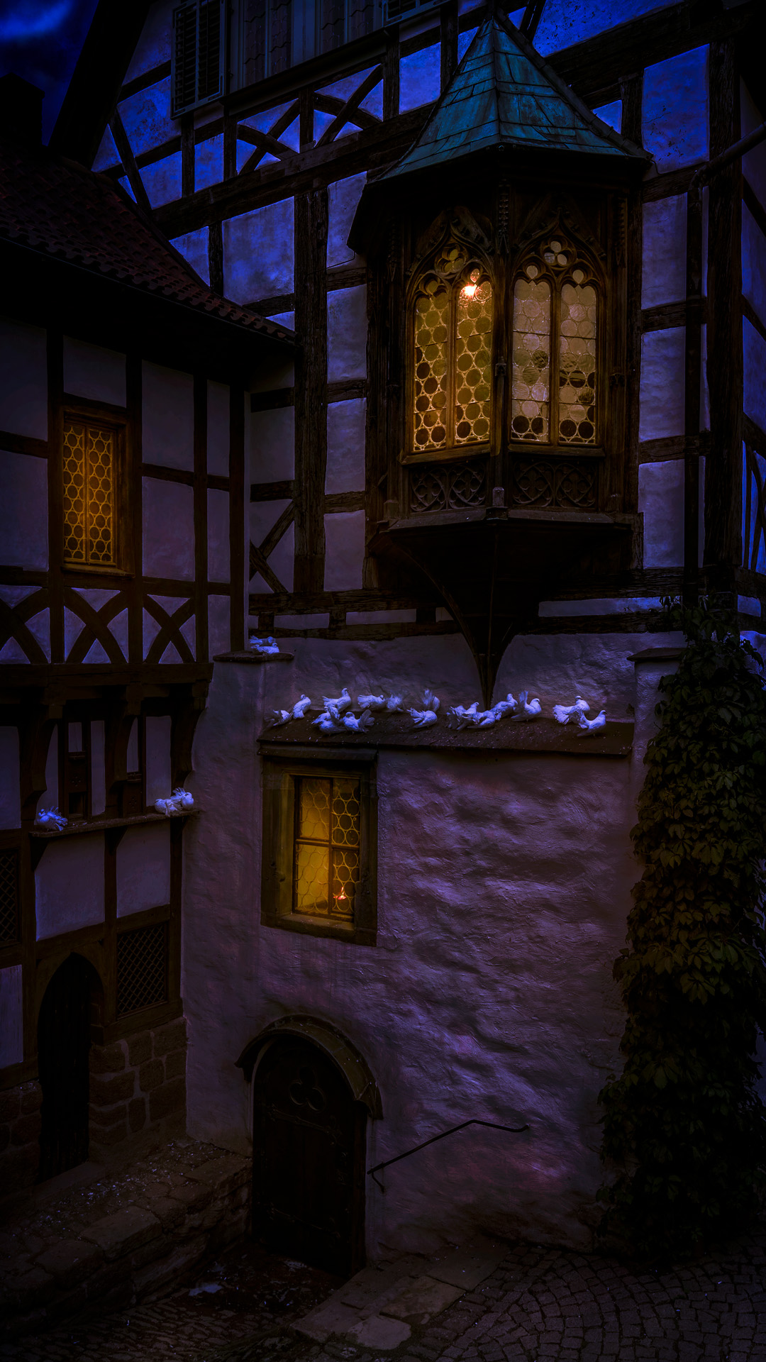Mittelalterlicher Erker der Wartburg bei Nacht mit leuchtenden Fenstern und weißen Tauben auf den Sims